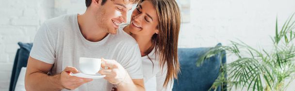 Horizontal crop of woman looking at boyfriend with cup of coffee - Фото, изображение