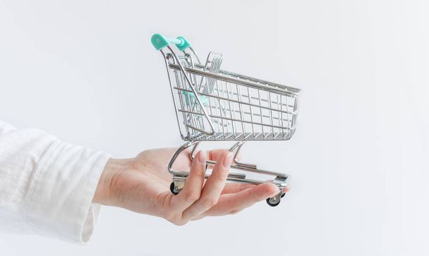 Mão feminina com carrinho de compras de brinquedo vazio sobre fundo branco. Conceito de compras. Espaço de cópia. - Foto, Imagem