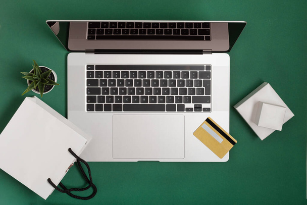 Tafel met laptop, smartphone, notebook en gouden credit card bovenaanzicht op groene achtergrond. Online winkelen concept. Modern interieur. - Foto, afbeelding