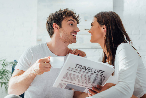Selektiver Fokus des Mannes, der eine Tasse Kaffee und Zeitung in der Hand hält, während er seine Freundin zu Hause anschaut  - Foto, Bild