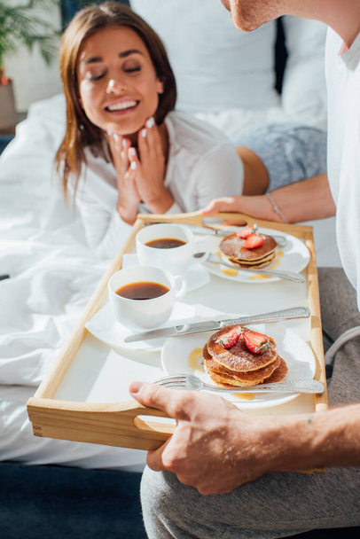 Selective focus of man holding breakfast on tray near woman on bed  - Foto, immagini