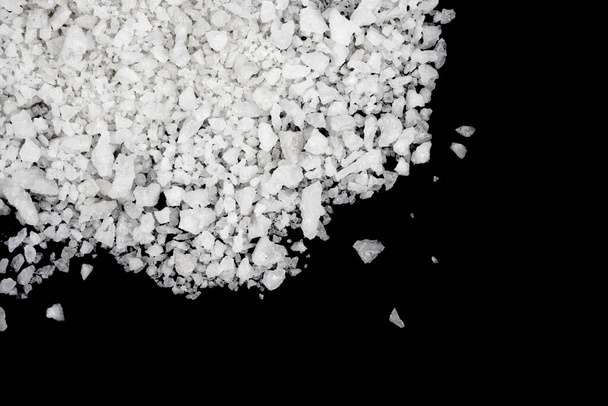Spilled white sea salt isolated black background. Clear crystalline shaker pebbles on a black background, macro, close up - Foto, imagen