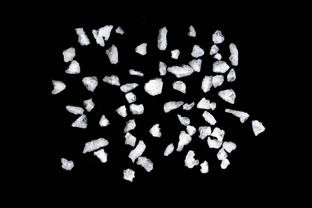 Spilled white sea salt isolated black background. Clear crystalline shaker pebbles on a black background, macro, close up - Photo, Image