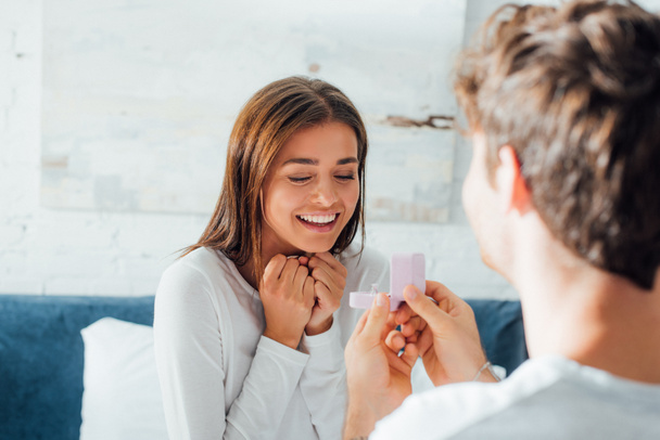 Selectieve focus van man holding box met sieraden ring tijdens huwelijksaanzoek in de buurt van vrouw in slaapkamer  - Foto, afbeelding