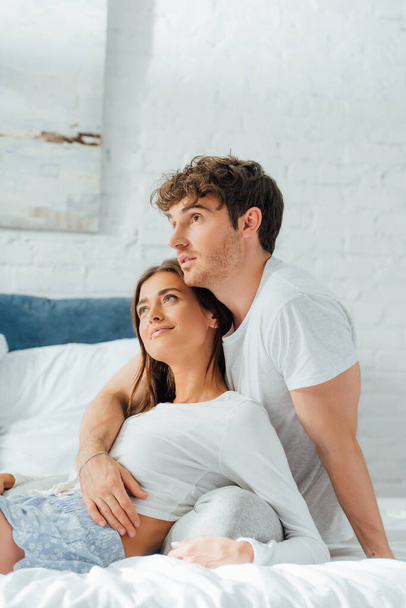 Young man hugging girlfriend in pajamas on bed at morning  - Фото, зображення