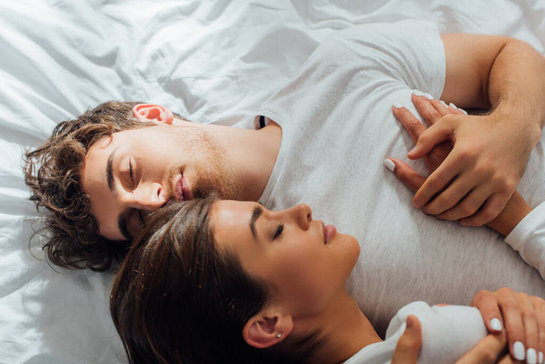 Top view of young couple embracing with closed eyes on bed  - Fotografie, Obrázek