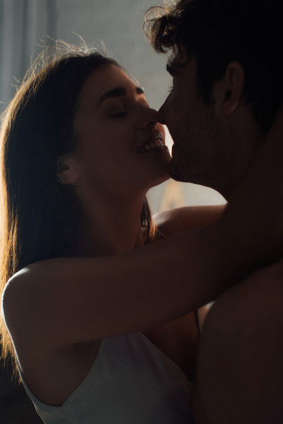 Jeune femme embrassant petit ami torse nu à la maison le soir  - Photo, image