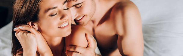 Horizontaal beeld van shirtloze man aanraken schouder van vriendin op bed  - Foto, afbeelding