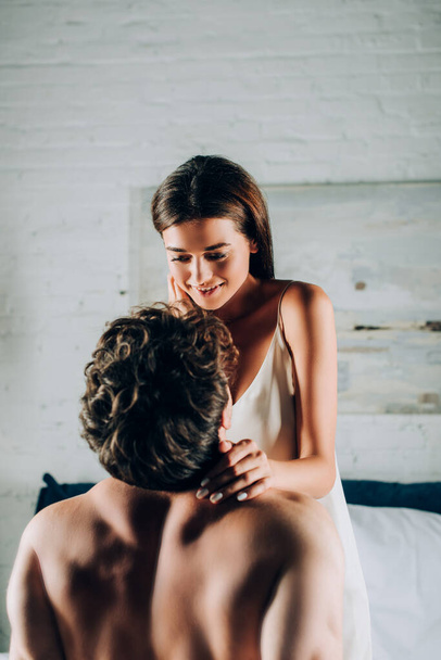 Shirless man aanraken verleidelijke vrouw in satijn nachtjapon op bed  - Foto, afbeelding