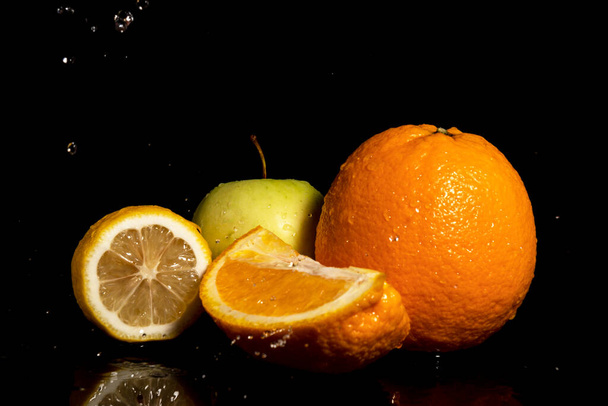 Appels en sinaasappelen met druppels en plons water op een zwarte achtergrond - Foto, afbeelding