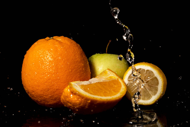 Apples and oranges fruits with drops and splashes of water on a black background - Photo, Image