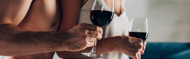 Panoramic crop of muscular man holding glass of wine near woman at home  - Foto, Bild