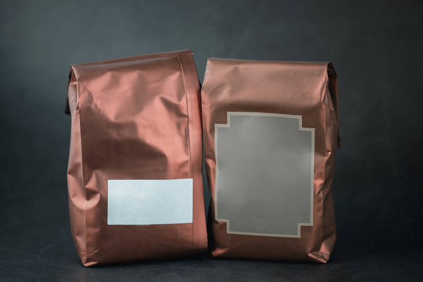 Alüminyum folyo, kakao tozu veya siyah arkaplanda kahve çekirdekleri için bakır renkli poşetler. - Fotoğraf, Görsel