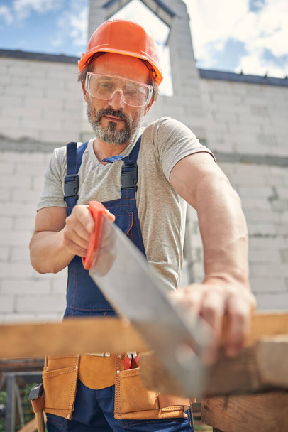 Trabalhador masculino focado usando uma serra manual - Foto, Imagem