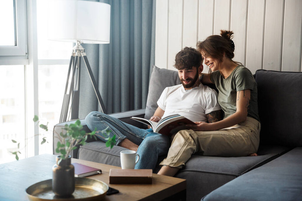 Lovely young couple relaxing on a couch at home, reading magazine - Foto, imagen