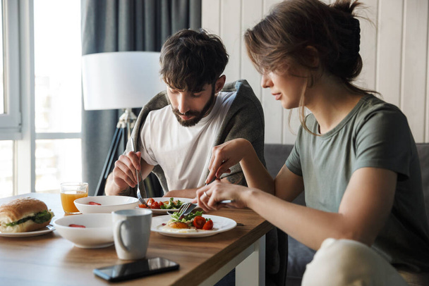 Lovely young couple having healthy breakfast in the kitchen, talking - Foto, afbeelding