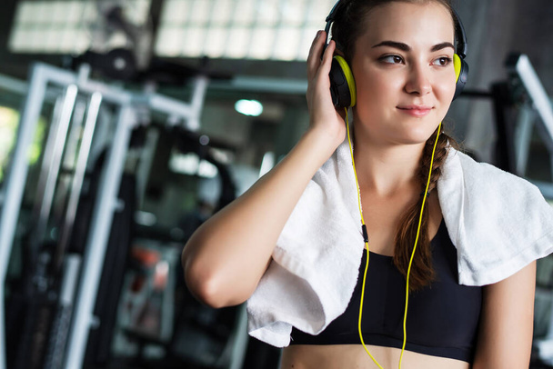 Young attractive woman listening to music by earphones connect to smart phone or cellphone. Relaxation after hard workout in gym   - Fotografie, Obrázek