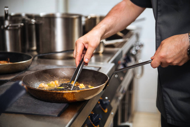 Σεφ μαγείρεμα μαύρο σπαγγέτι σε ένα τηγάνι με λαβίδες - Φωτογραφία, εικόνα