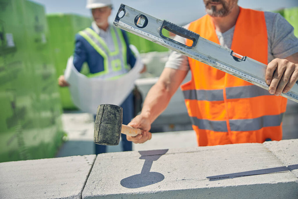 Constructor sosteniendo un martillo de ladrillo y nivel de espíritu - Foto, Imagen