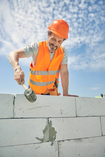 Uśmiechnięty murarz z narzędziem budowlanym na zewnątrz - Zdjęcie, obraz