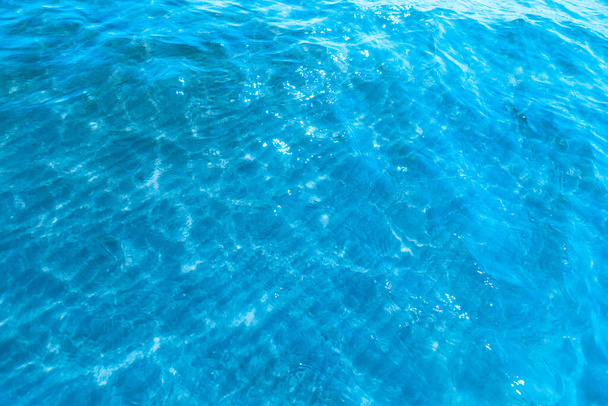  Sahilin arka planında mavi şeffaf deniz suyu. Güneşli bir günde hafif dalgalar ve parlayan temiz su yüzeyi. deniz tatili - Fotoğraf, Görsel