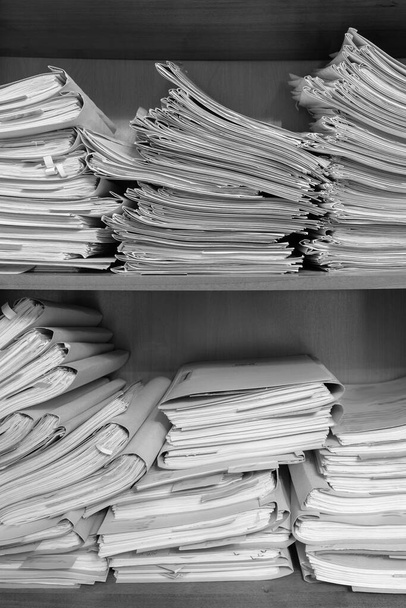Papierdokumente stapeln sich im Archiv. Dokumente in den Regalen des Archivraums. Büroregale im Schrank voller Akten. Schwarz-Weiß-Foto - Foto, Bild