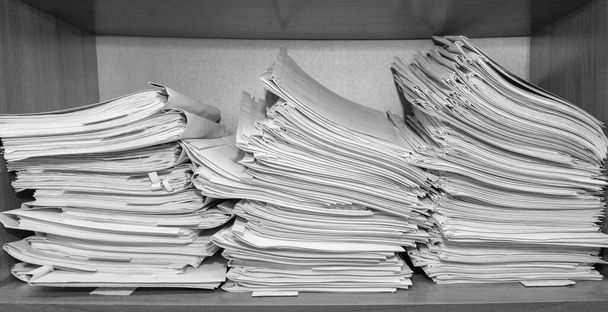 Papieren documenten opgestapeld in het archief. Documenten op de planken van de archiefkamer. Kantoorplanken in de kast vol met bestanden. zwart-wit foto - Foto, afbeelding