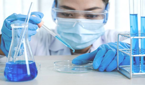 Naukowcy trzymają pipetę i upuszczają niebieski płyn chemiczny do badań i analiz w laboratorium.. - Zdjęcie, obraz