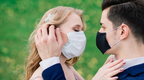 Giovane coppia amorevole a piedi in maschere mediche nel parco durante la quarantena il giorno del loro matrimonio. Coronavirus, malattia, protezione, malattia. Celebrazione Europa annullata. - Foto, immagini