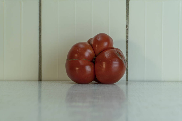 Tři ošklivé červené rajče leží na stole a je v něm reflex. Domácí zelenina je dobrá pro zdravou výživu, protože obsahuje mnoho vitamínů a mikroprvků. Vodorovný obrázek, vysoká klávesa. - Fotografie, Obrázek