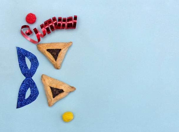 Háromszögletű sütik mákos magvakkal (hamantasch vagy aman fülekkel), cukorkával, csillámos maszkkal, szerpentinnel a purim zsidó nyaralásához - Fotó, kép