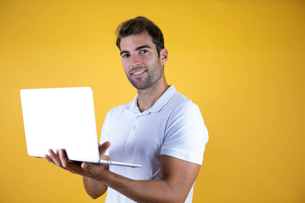młody pracownik człowiek działa za pomocą laptopa stojącego na żółtym tle bardzo skoncentrowany. - Zdjęcie, obraz