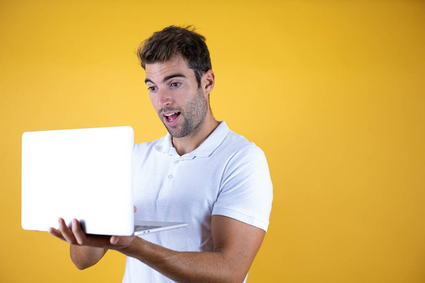 Молодий працівник працює за допомогою ноутбука, що стоїть над жовтим тлом, дуже вражений
. - Фото, зображення