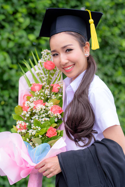 Afgestudeerde vrouwelijke studenten dragen afstudeerhoed en toga met geluk gevoel met park achtergrond - Foto, afbeelding