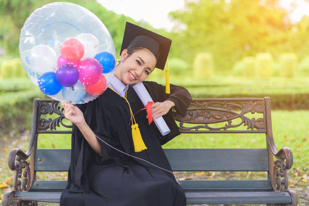 Absolwentka, studentka nosząca kapelusz i suknię dyplomową z poczuciem szczęścia w tle parku - Zdjęcie, obraz