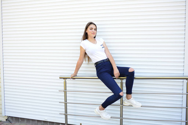 Beautiful young woman wearing jeans, white t-shirt, standing on the street. photo near iron fence. - Foto, Bild
