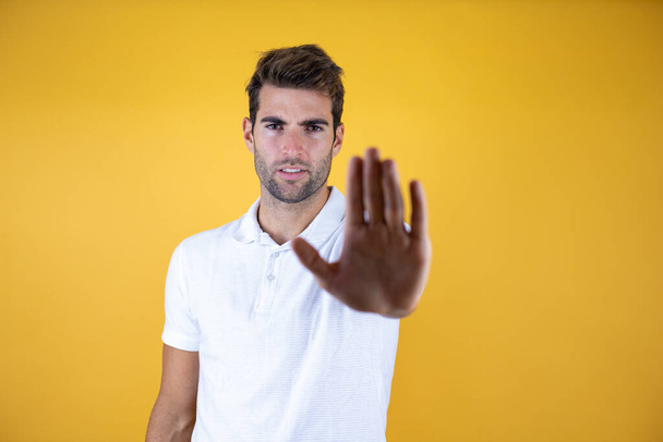 Jeune homme beau sur fond jaune isolé avec la main ouverte faisant stop signe avec expression sérieuse et confiante, geste de défense - Photo, image