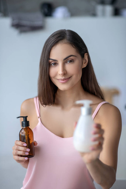 Pretty long-haired woman holding bottles with body lotion - Фото, зображення