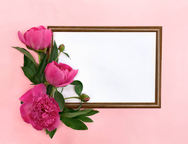 Ramo de peonías rosadas con marco de foto sobre un fondo de papel rosa con espacio para el texto. Vista superior, cama plana. Decoración floral - Foto, imagen