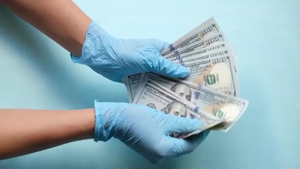 Ręce w rękawiczkach medycznych liczą pieniądze na niebieskim tle. Lekarze liczą pieniądze. Pojęcie korupcji lub kosztownej opieki zdrowotnej. - Materiał filmowy, wideo