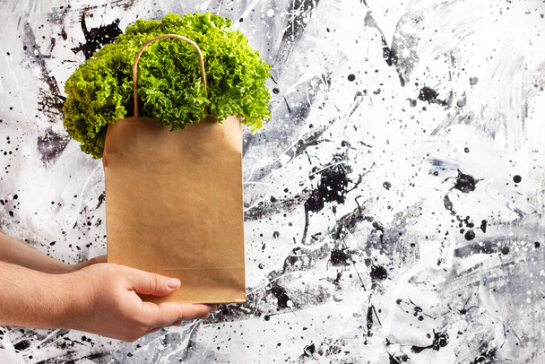 Main tenant mélange de salade fraîche dans un emballage écologique sur un fond blanc et noir.Livraison de nourriture.Manger sainement - Photo, image