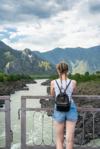 Young woman standing on a bridge over a mountain river. Wonderful mountain landscape. Long distance travel. Happiness alone with nature. - Фото, зображення