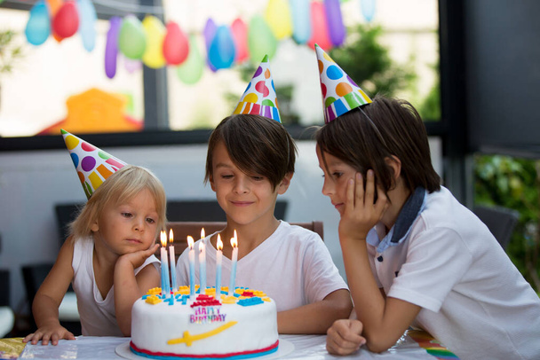 Adorable niño feliz, niño pequeño celebrando su cumpleaños en casa con globos, hermanos y pastel casero colorido - Foto, imagen