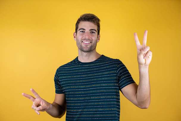 handsome man standing over isolated yellow background smiling and doing the ok signal with thumbs - Photo, Image
