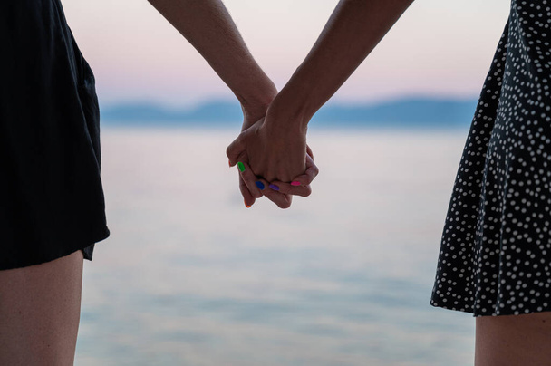 Nahaufnahme eines lesbischen schwulen Paares, das die Hände am Abendmeer hält. - Foto, Bild
