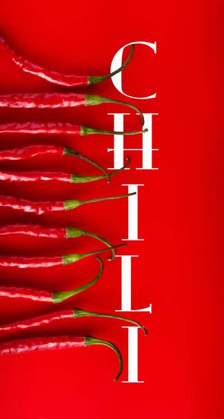 Eleven Red Chilies (viewed in half) in a row on red background.  With text chili. Overhead shot - Photo, Image