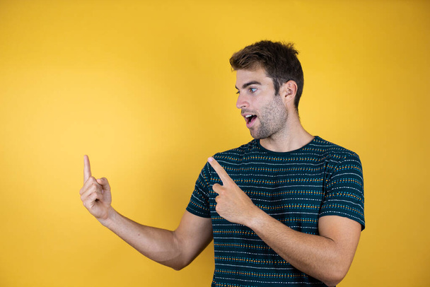 Fiatal jóképű férfi elszigetelt háttér csodálkozva mutat oldalra két ujjal - Fotó, kép