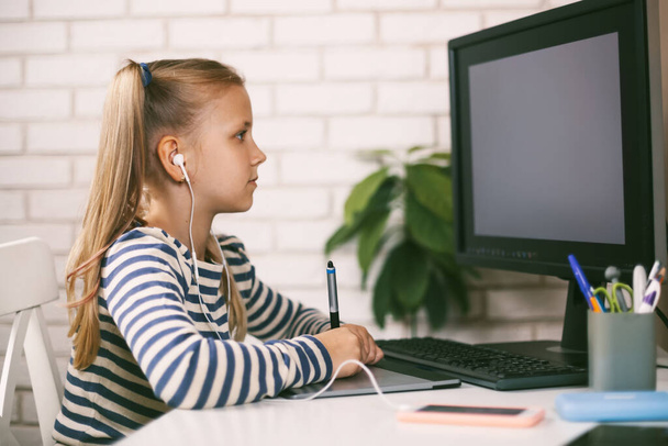 Una ragazza in cuffia si siede a un tavolo al computer a casa e fa i compiti Educazione online. Il bambino impara da casa. - Foto, immagini