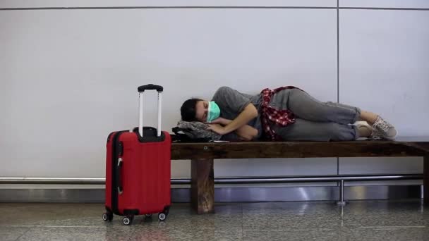 彼女の顔に医療マスクをした気違いの、ストレスの多い、疲れた少女の旅行者は、コロナウイルスのために乗り遅れ、またはキャンセルされたフライトを待っています。covid-19のため空港で夜を過ごす乗客 - 映像、動画