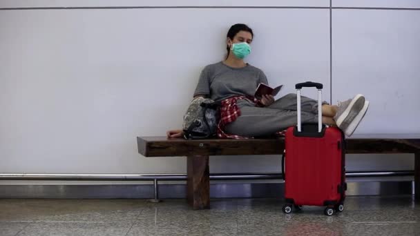 Distraught, stressed, tired girl traveler with a medical mask on her face is waiting for missed, delayed or canceled flight due to a coronavirus. Passenger spending a night at airport due to covid-19 - Footage, Video